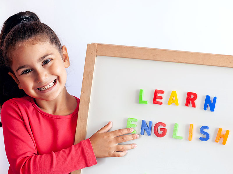 "Young girl holding a board with magnetic letters spelling 'learn English'"